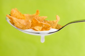 spoon with corn flakes on green background