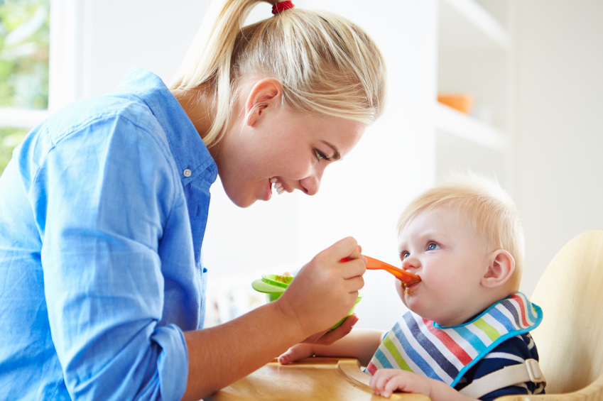 Mother Feeding Baby Boy In High Chair