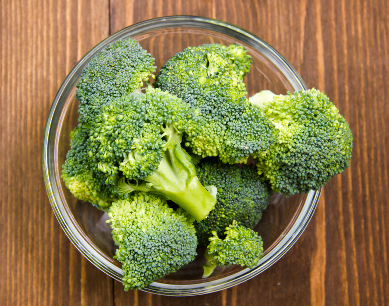 Broccoli in glass bowl on wooden table seen from above