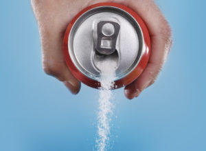 hand holding soda can pouring a crazy amount of sugar in metaphor of sugar content of a refresh drink isolated on blue background in healthy nutrition, diet and sweet addiction concept