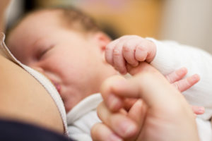 Newborn baby holding mother finger and breastfeeding.