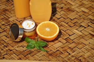 Orange face cream with half of orange and bottles of lotion and shower gel in background, on wooden surface