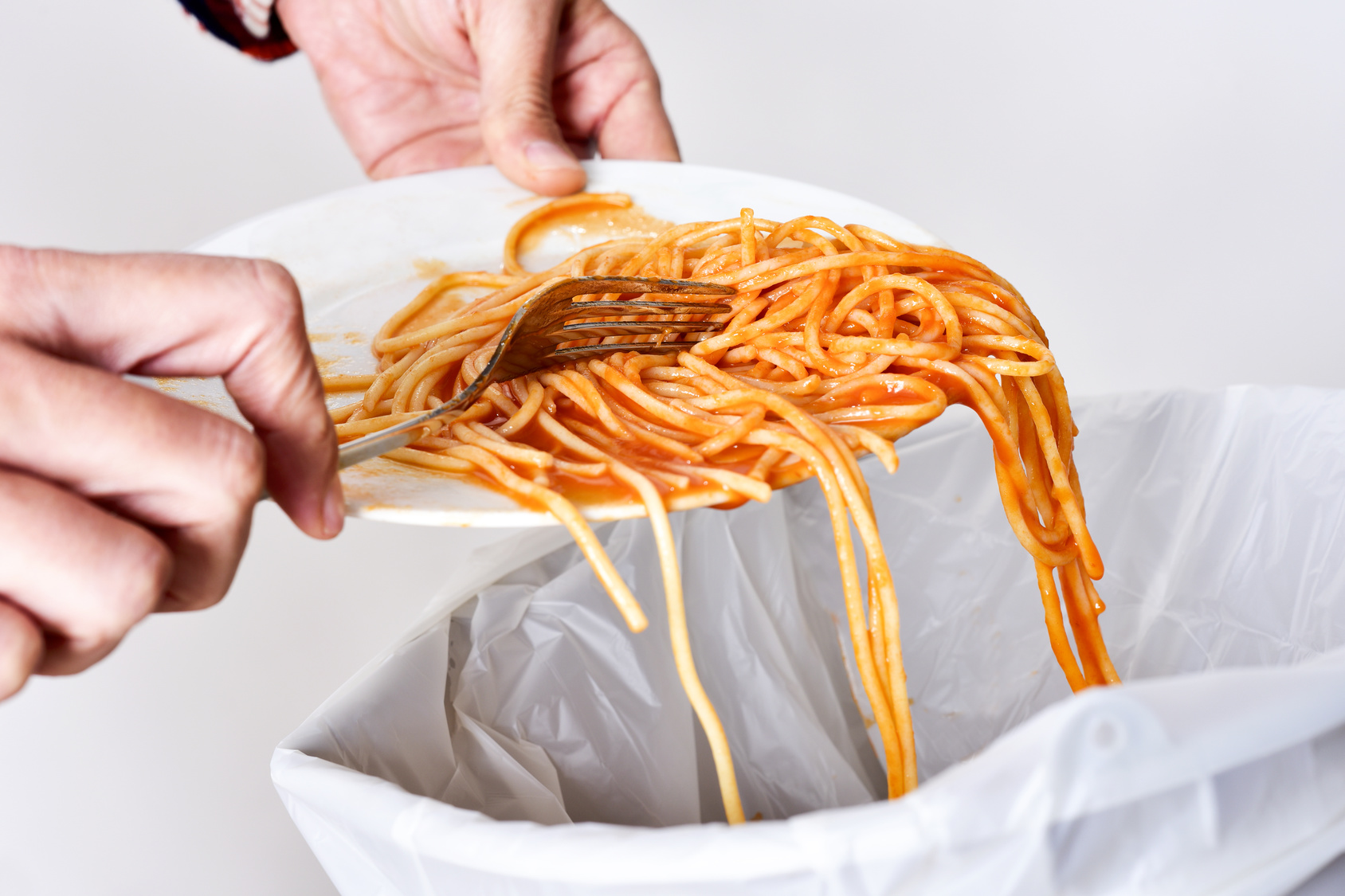closeup of a young man throwing the leftover of a plate of spaghetti to the trash bin