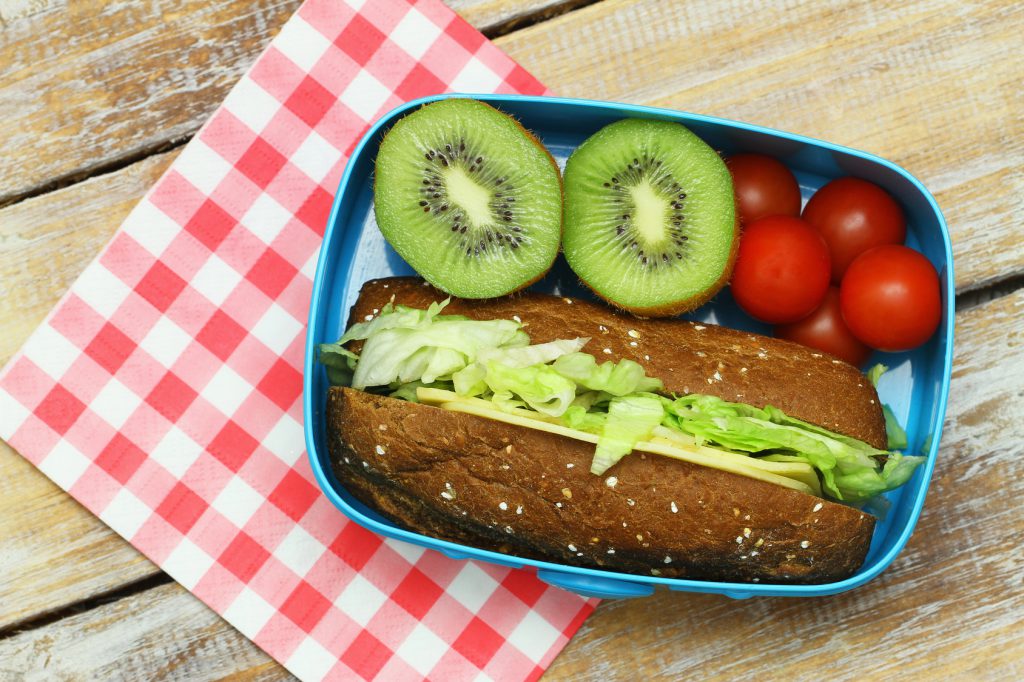 Healthy lunch consisting of brown cheese and lettuce roll, cherry tomatoes and kiwi fruit