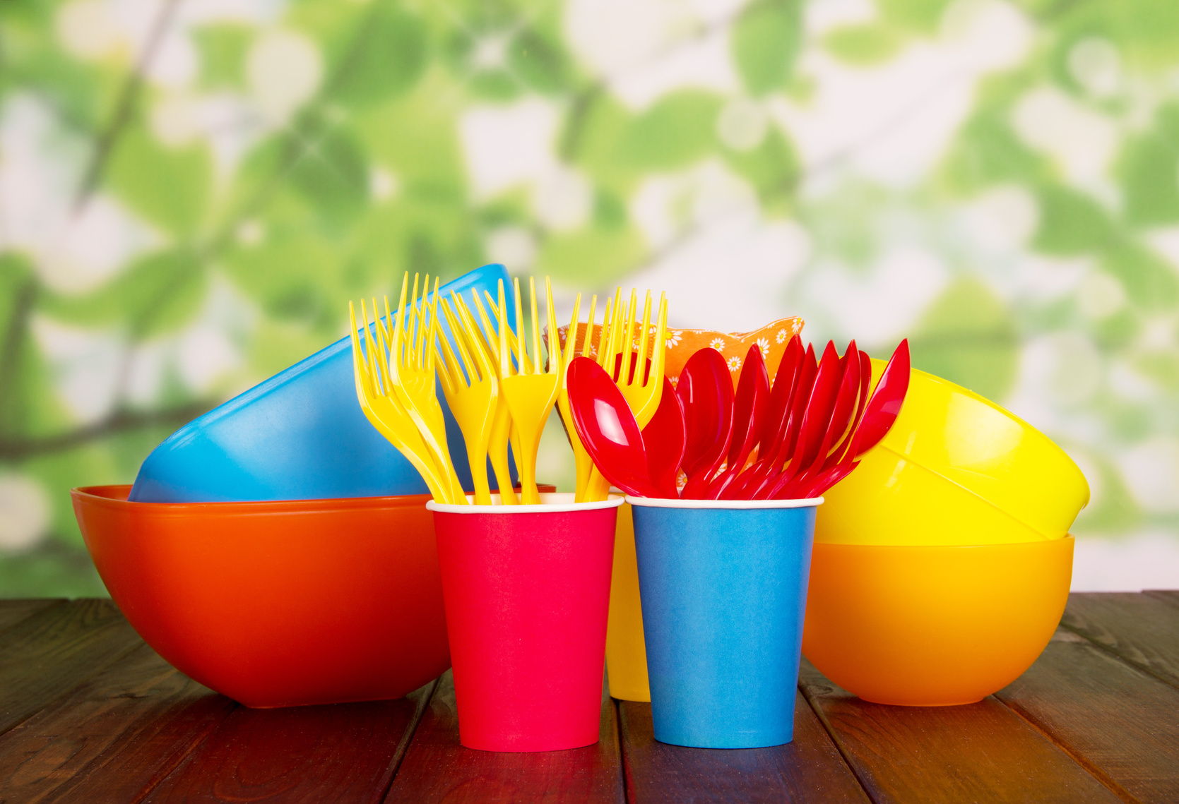 Colored plastic tableware: bowls, forks, spoons on abstract green .