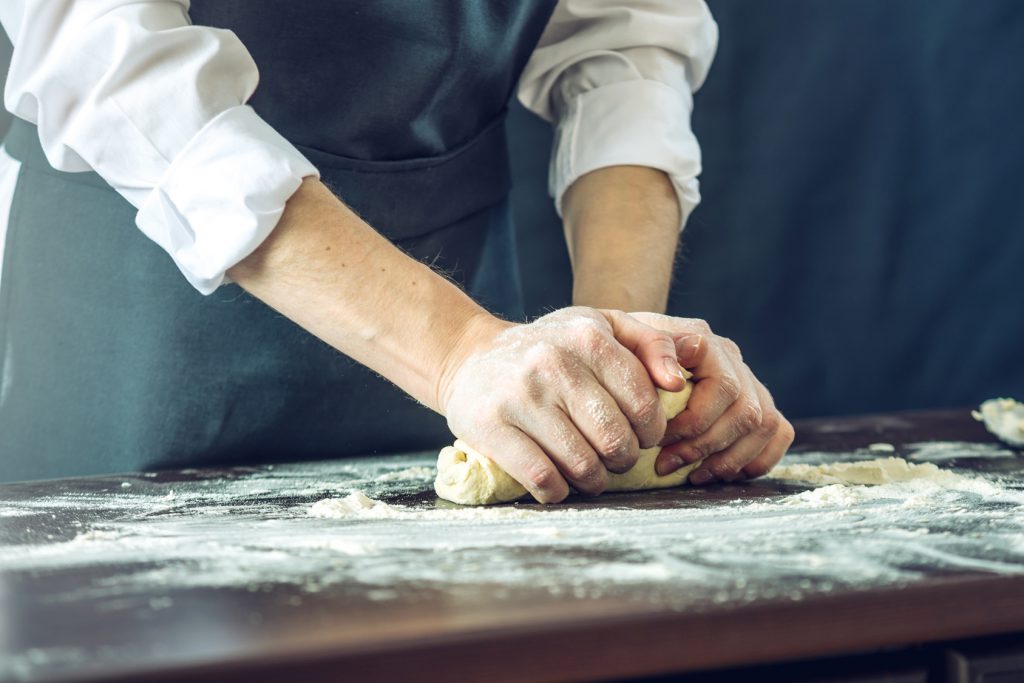 The chef in black apron makes pizza dough with your hands on the table